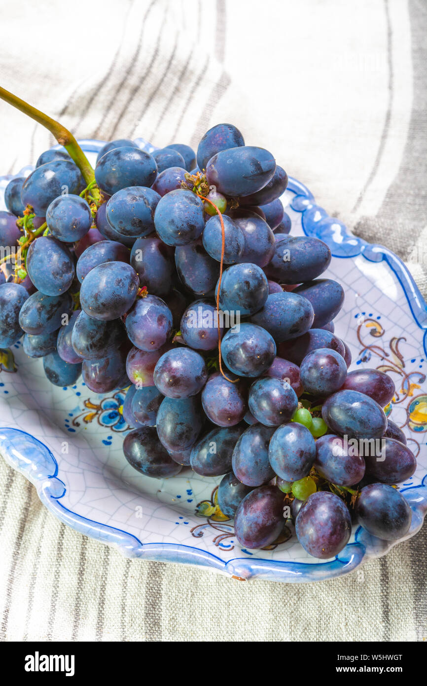 Bande de couleur bleu-noir à maturité des raisins de table avec feuille servi sur plaque bleue comme dessert de fruits doux Banque D'Images