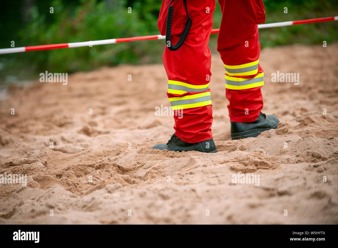 Les jambes de sauveteur standind sur le sable en face de ruban rouge et blanc. Pantalon rouge avec des éléments réfléchissants. Banque D'Images