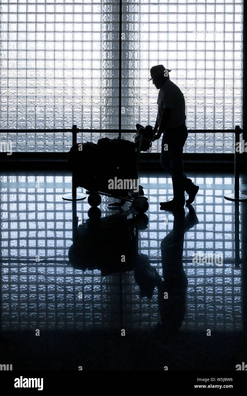 Silhouette d'un genteman poussant un chariot chargé avec assurance à travers l'aéroport Banque D'Images