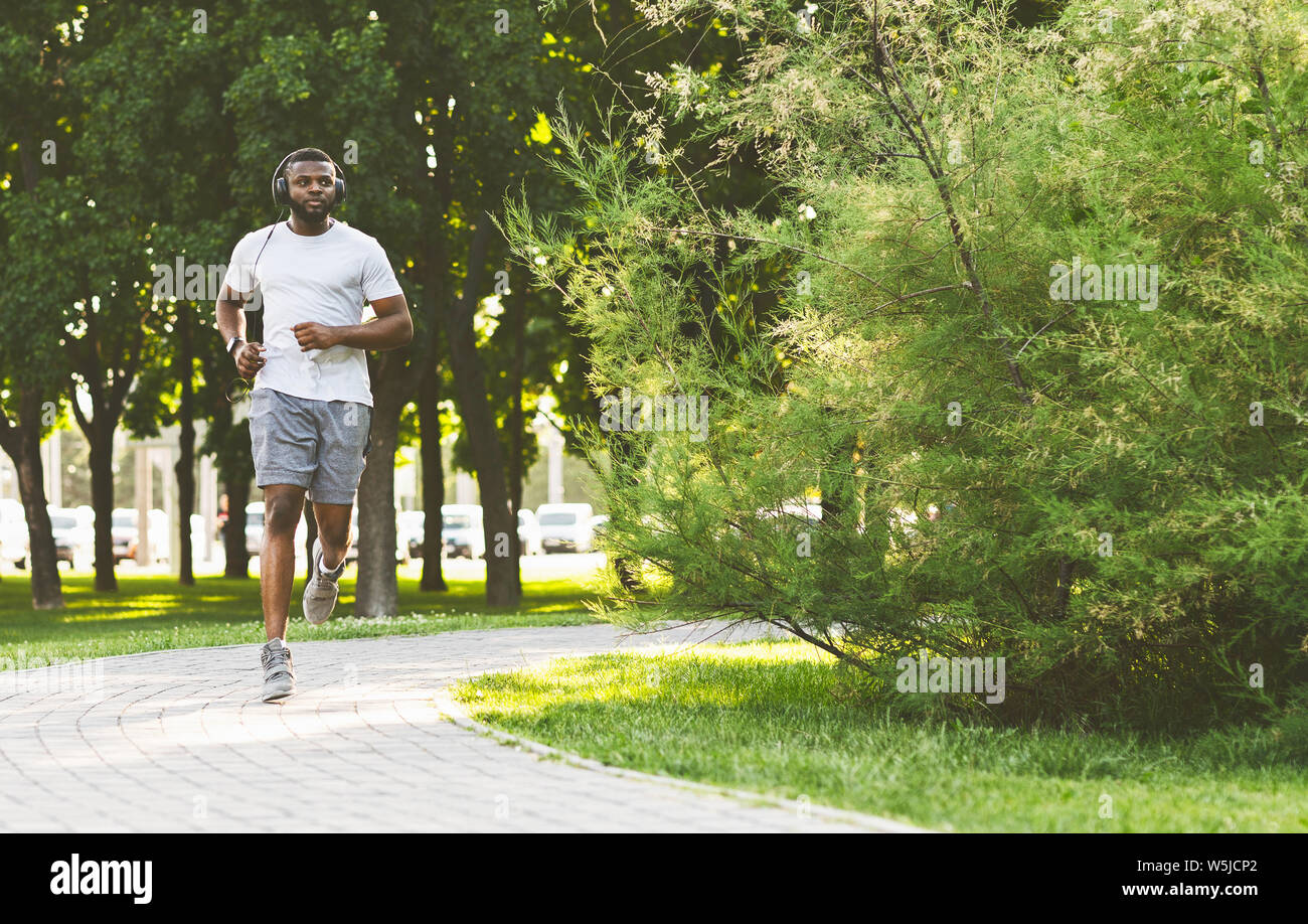 Guy afro sportive avec casque est courir dans le parc Banque D'Images