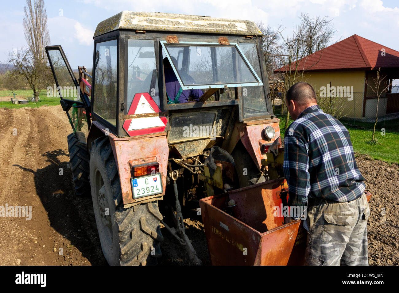 Deux hommes jeunes semis de pommes de terre avec l'aide d'un tracteur dans les régions rurales de la Slovaquie. Banque D'Images
