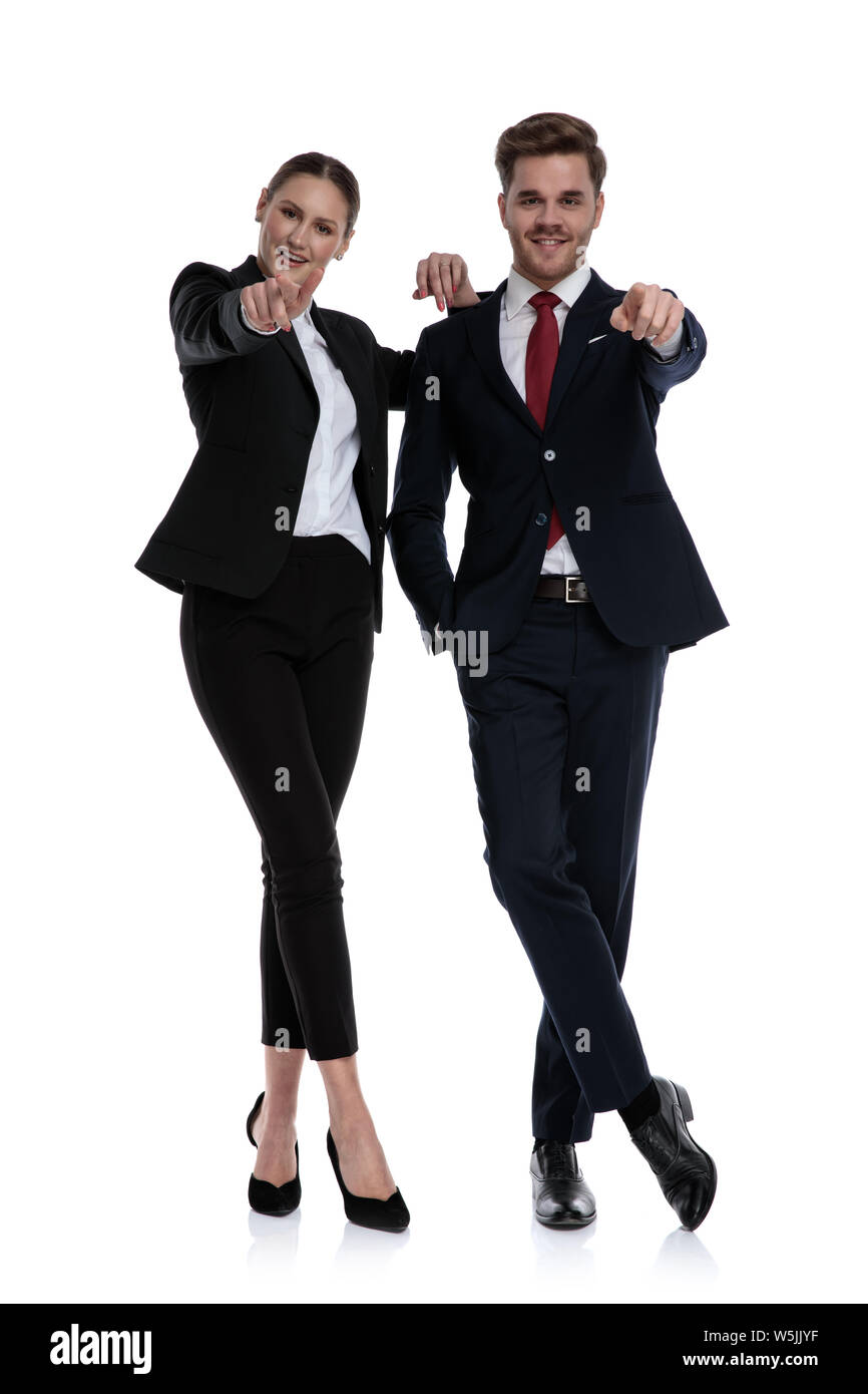 Couple dans les complets pointant en position debout avec les jambes croisées sur fond blanc Banque D'Images