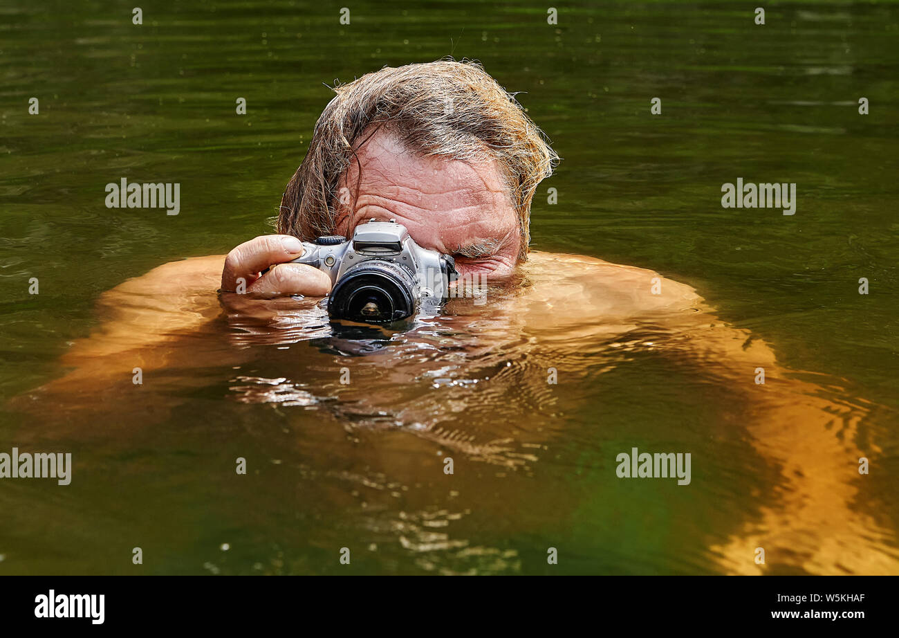 Homme mature fait du voyeurisme à la surface de l'eau de la rivière avec l'aide de l'appareil photo imperméable dans ses mains. Banque D'Images