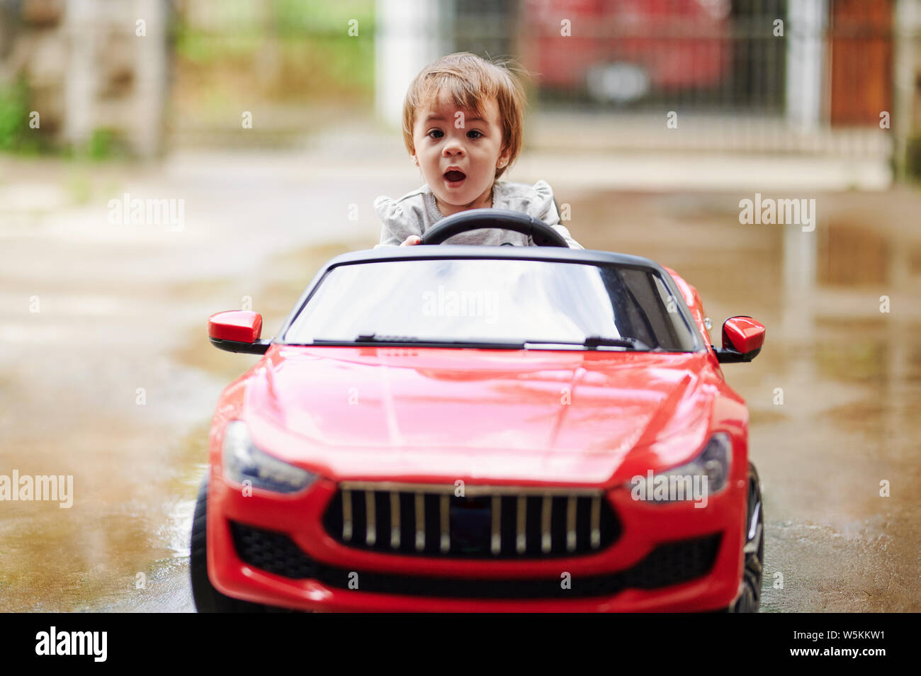 Petite fille petite voiture conduite sur le parc extérieur flou Banque D'Images