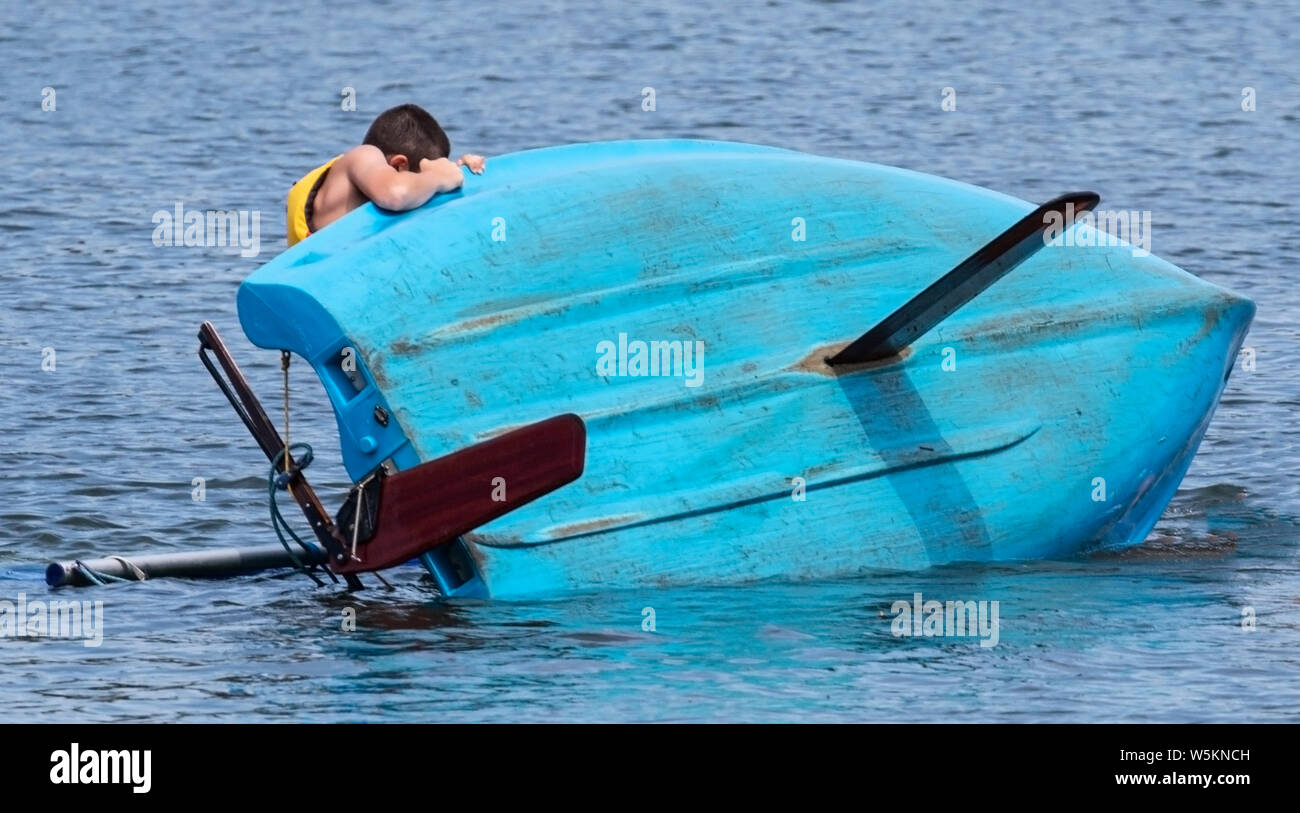 Un homme youn tente d'accrocher à son voilier après qu'il a chaviré dans l'eau. Banque D'Images