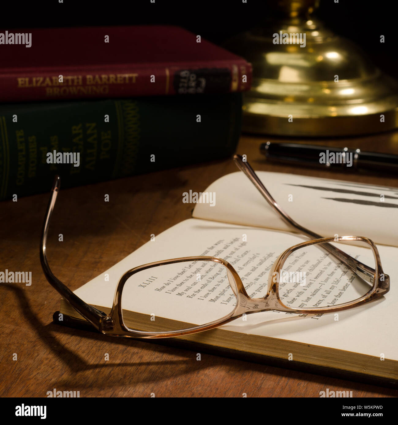 Une paire de lunettes portées à l'envers sur un livre ouvert, avec d'autres livres et d'un stylo d'encre sur un bureau avec une lampe en laiton. Banque D'Images
