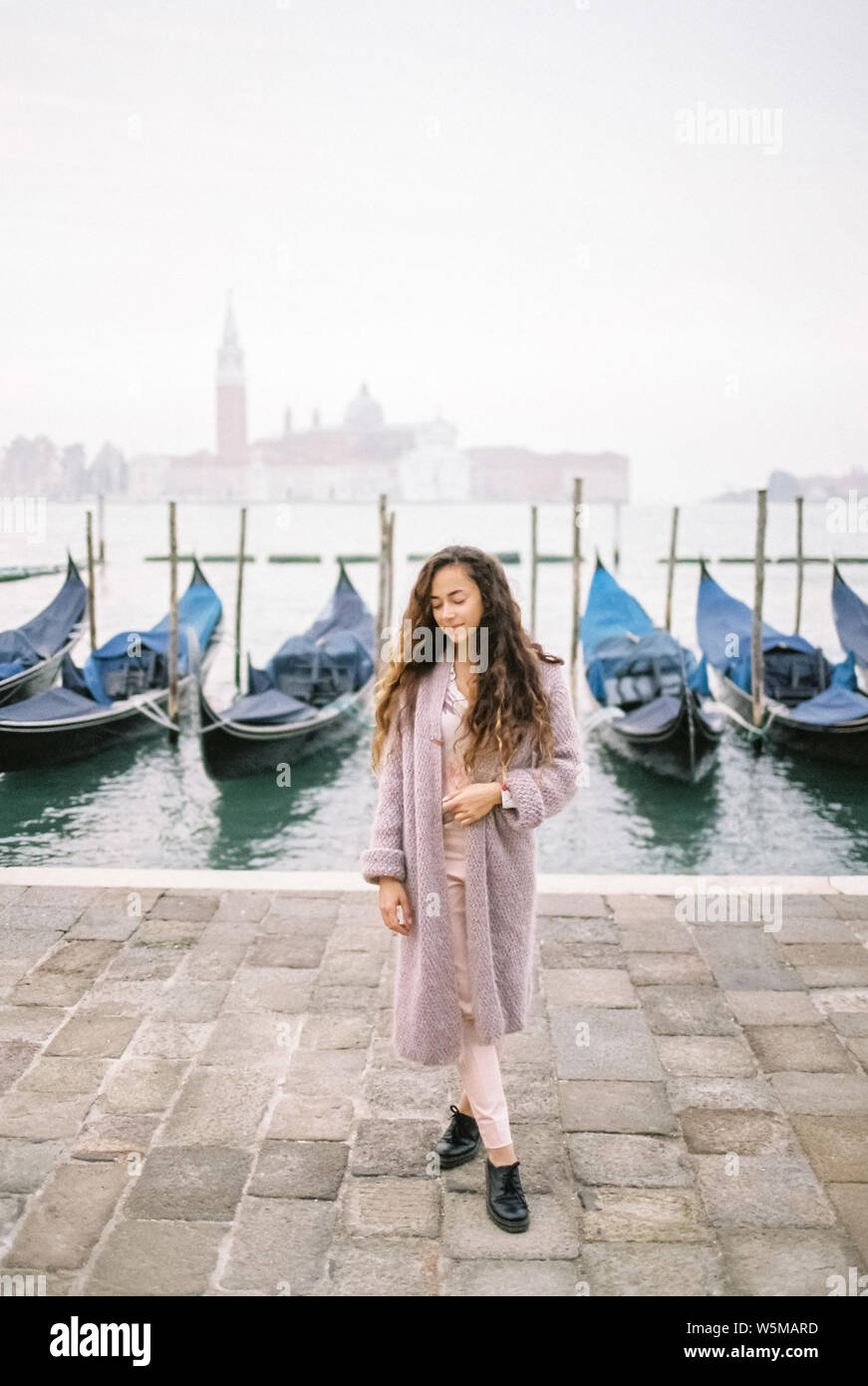 Femme dans le quartier branché d'automne look' avec vue sur la lagune de Venise avec les gondoles et San Giorgio Maggiore sur l'arrière-plan. Pull cape couleur corail. Italien célèbre Banque D'Images