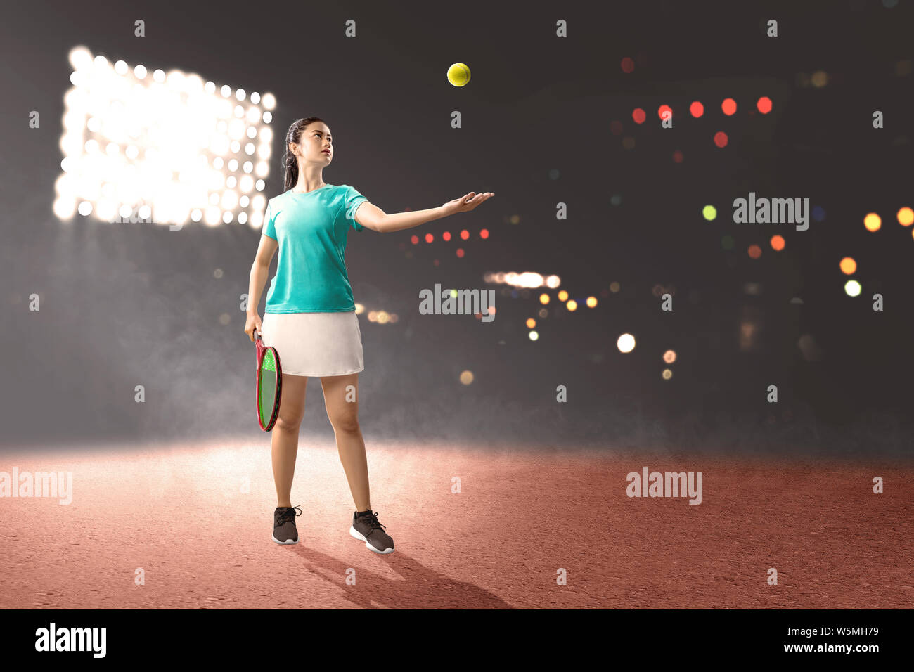 Femme Asiatique avec une raquette de tennis dans ses mains, prêt à servir de poste sur fond projecteurs Banque D'Images