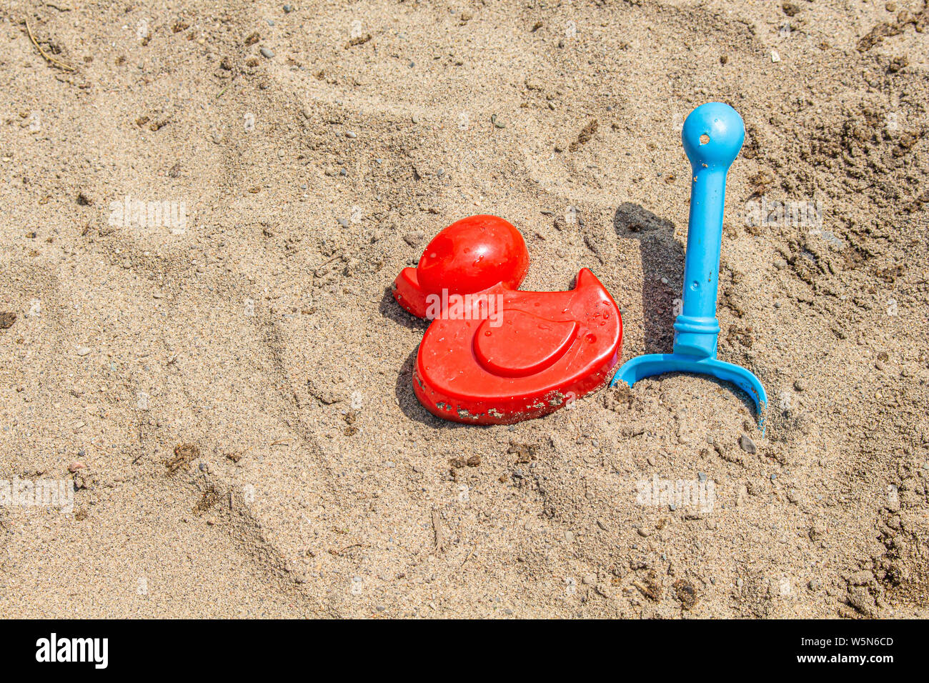 Les jouets de sable, un canard et un moule rouge pelle bleu, s'asseoir sur le sable d'une plage au soleil. Banque D'Images