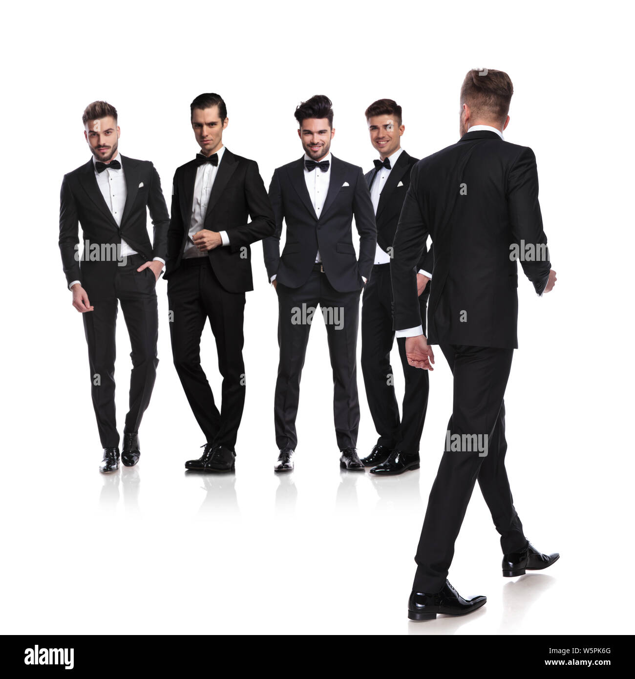 Cinq hommes habillés en tuxedoes avec leader rentrer à pied à côté et à les regarder, sur fond blanc, pleine longueur photo Banque D'Images