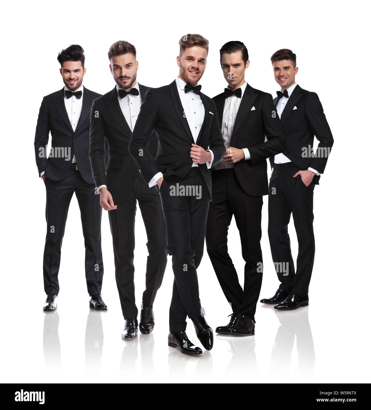 Équipe de cinq garçons vêtus de noir sur fond blanc permanent tuxedoes avec leader à l'avant, un corps entier photo Banque D'Images