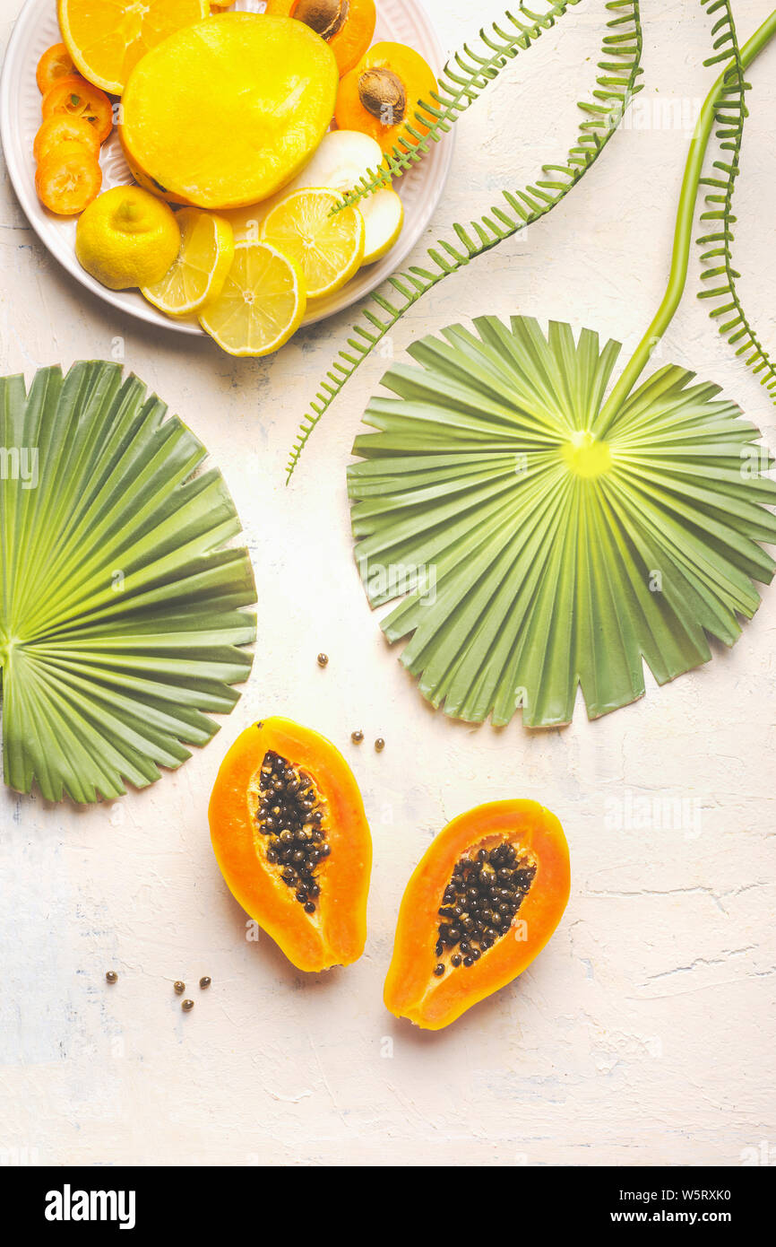 Papaye mûres coupées en deux avec les graines sur tableau blanc avec des feuilles tropicales et la plaque avec les fruits tranchés jaune, vue du dessus. L'alimentation d'été. L'alimentation saine. Br Banque D'Images