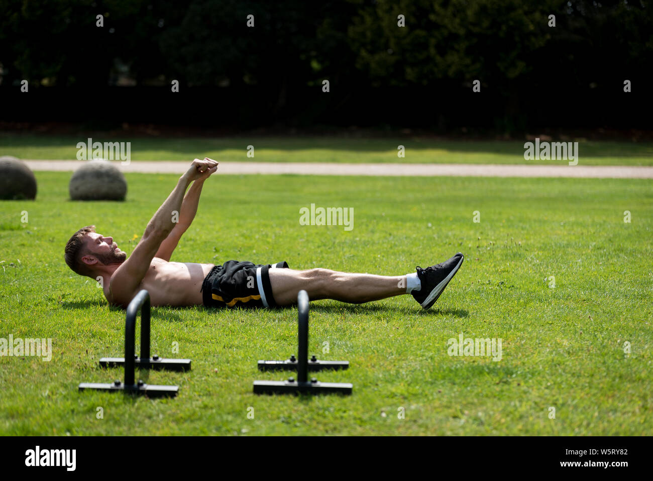 Man performing réchauffer avant de faire la gymnastique fitness workout dans un parc public en plein air, UK Banque D'Images