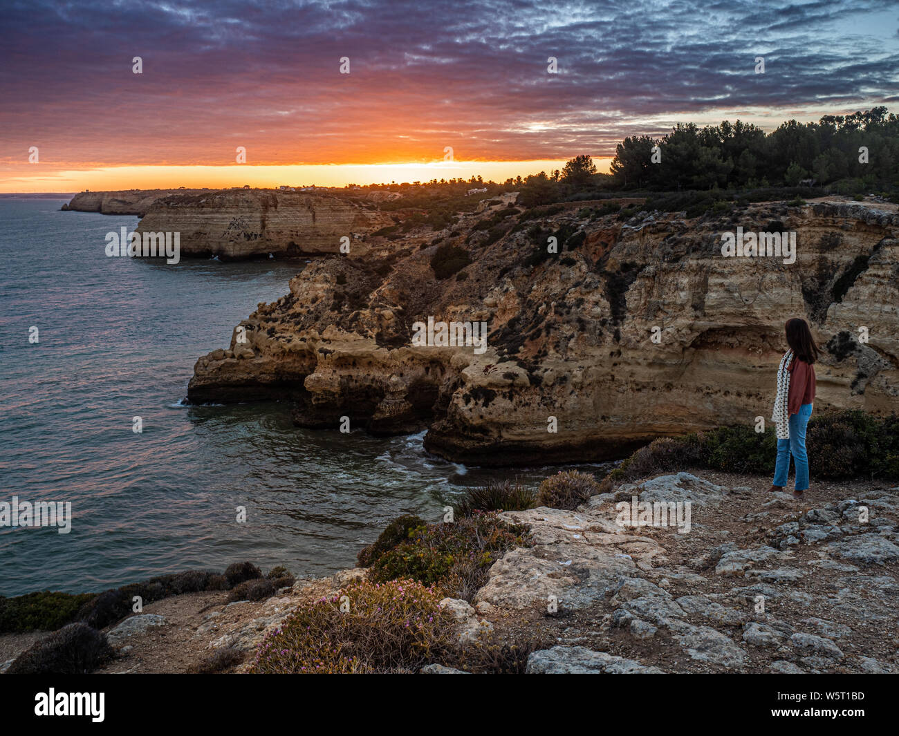 Une dame debout sur les falaises de l'Algarve à regarder le dernier de le coucher du soleil dans le ciel du soir Banque D'Images