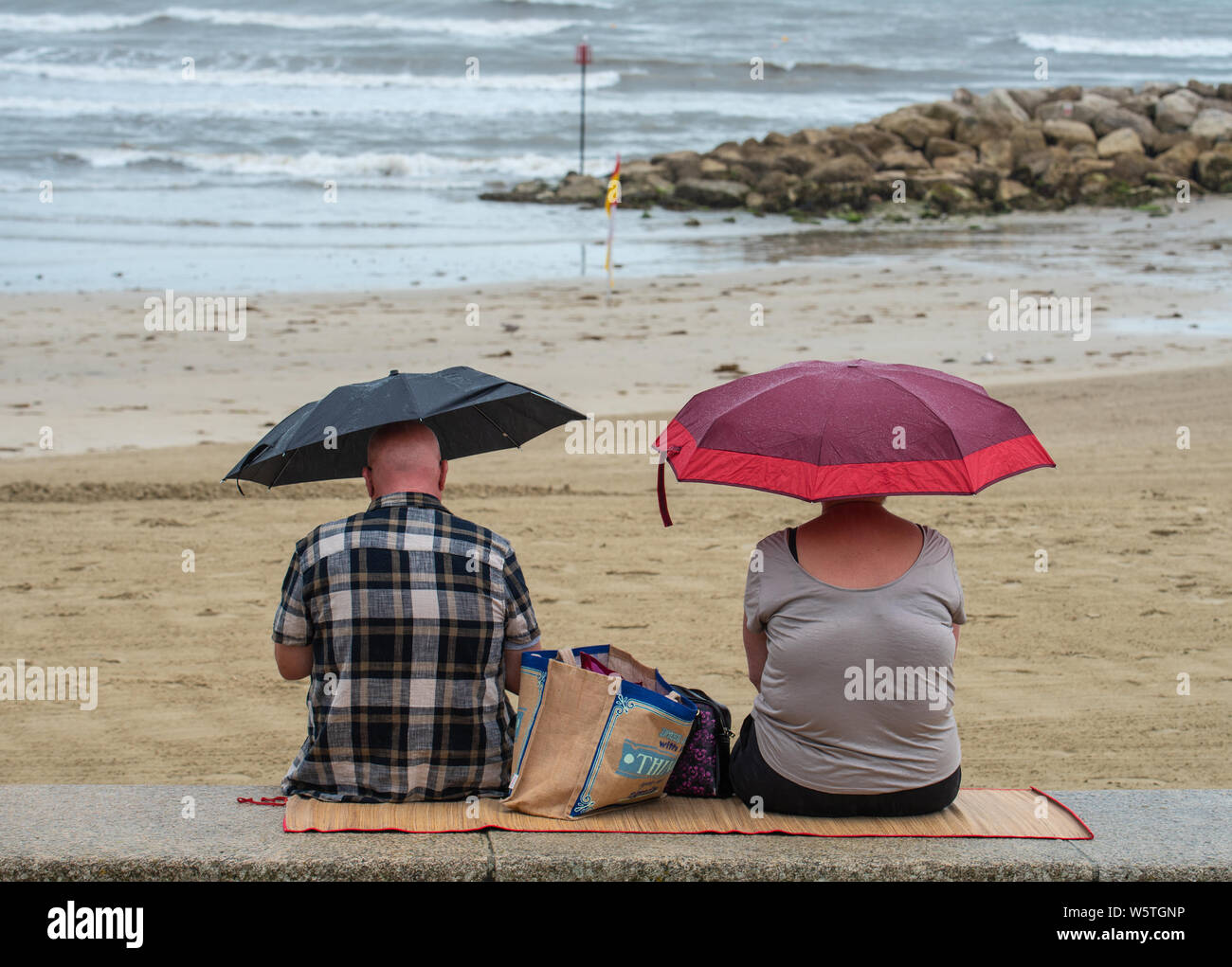Lyme Regis, dans le Dorset, UK. 30 juillet 2019. Météo France : Suite jours de soleil, de fortes averses de pluie a frappé la station balnéaire de Lyme Regis. Les visiteurs à l'abri sous des parasols sur une plage presque vide. Credit : Celia McMahon/Alamy Live News. Banque D'Images