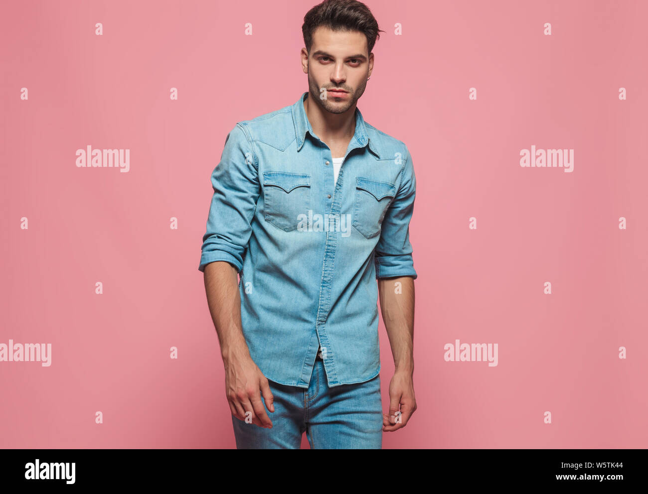 Portrait of handsome man wearing denim shirt à manches, debout sur fond rose Banque D'Images