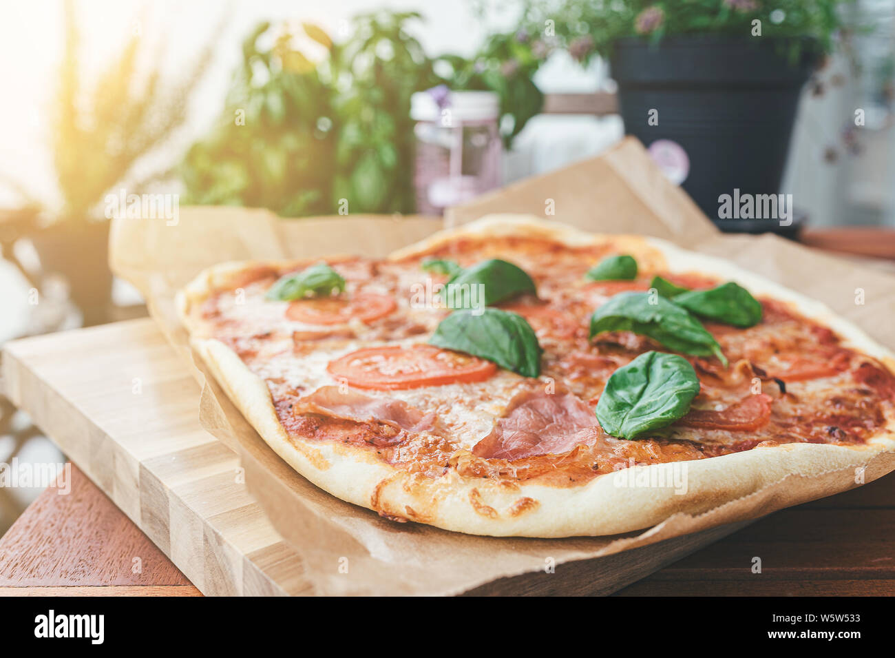 Des pizzas fraîches avec serrano, tranches de tomate et des feuilles de basilic frais sur table en bois on patio Banque D'Images