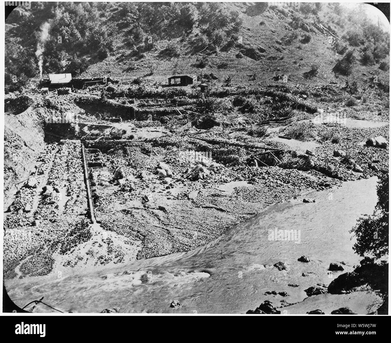 Photographie d'une exploitation minière de la rivière avec une partie de l'eau détournée pour le filtrage et le tri de l'or. Une écluse avec plusieurs hommes travaillent le long du côté de il peut être vu sur la gauche de l'photgraph. ; la portée et contenu : le campement non identifié comme est le courant lui-même. C'était probablement situé dans la Sierra Nevada gold mining district. Banque D'Images