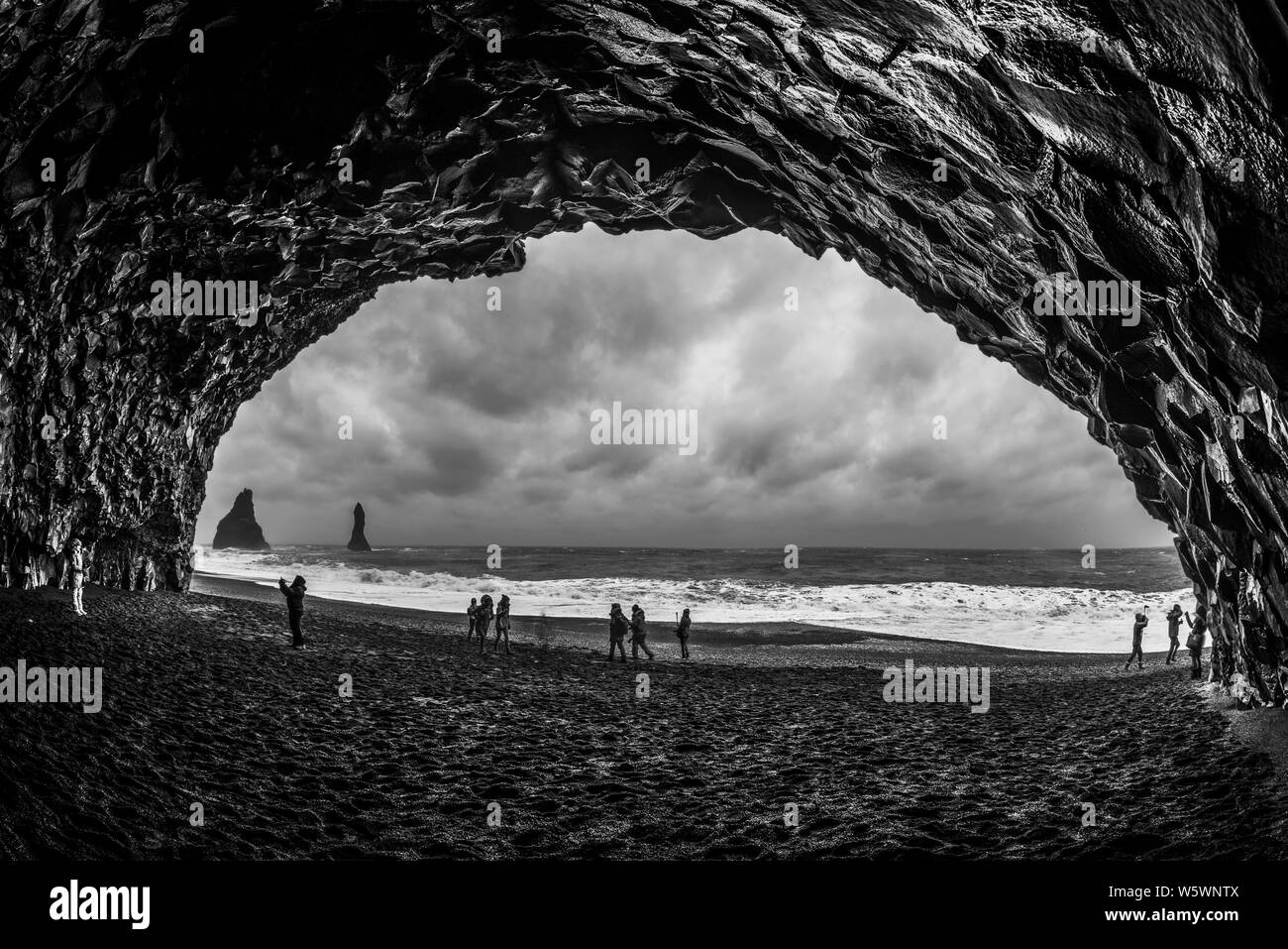 Les touristes à la découverte de rares formations grotte rocheuse dans la plage de sable noir, l'Islande Banque D'Images