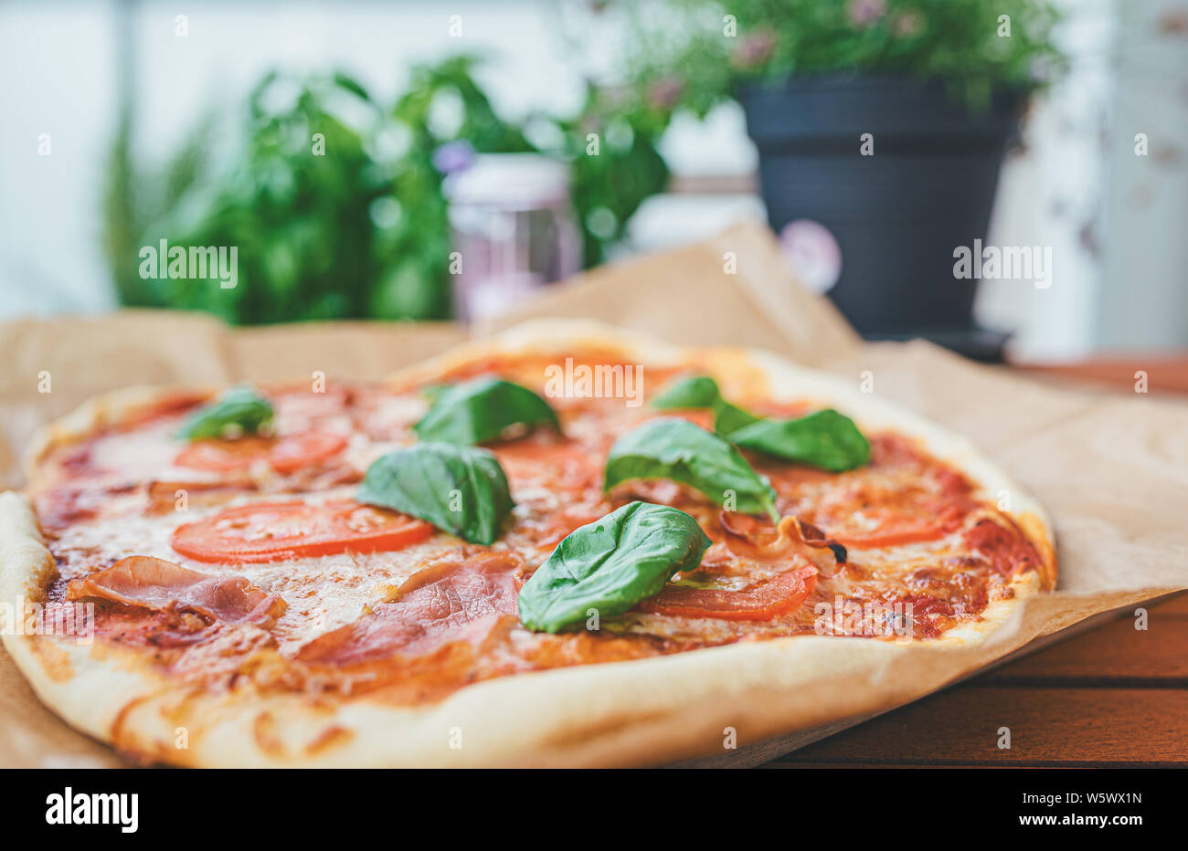 Des pizzas fraîches avec du jambon serrano, des tranches de tomate et des feuilles de basilic frais sur table en bois on patio Banque D'Images