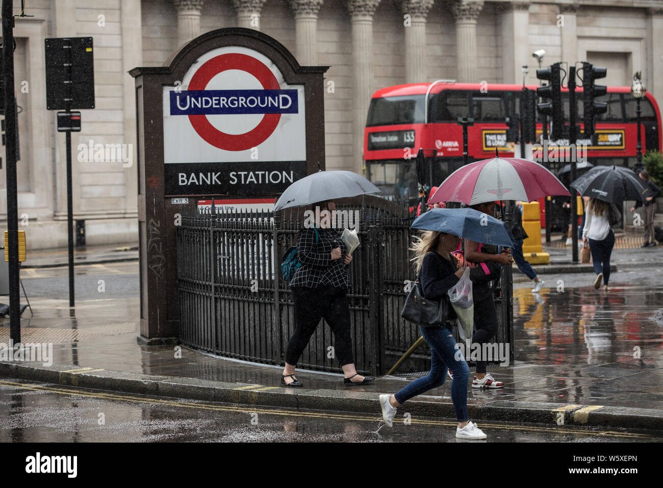 Les touristes avec des parasols à l'abri d'une averse de pluie lourde à pied de la station de métro Bank dans la ville de Londres, Angleterre, Royaume-Uni Banque D'Images