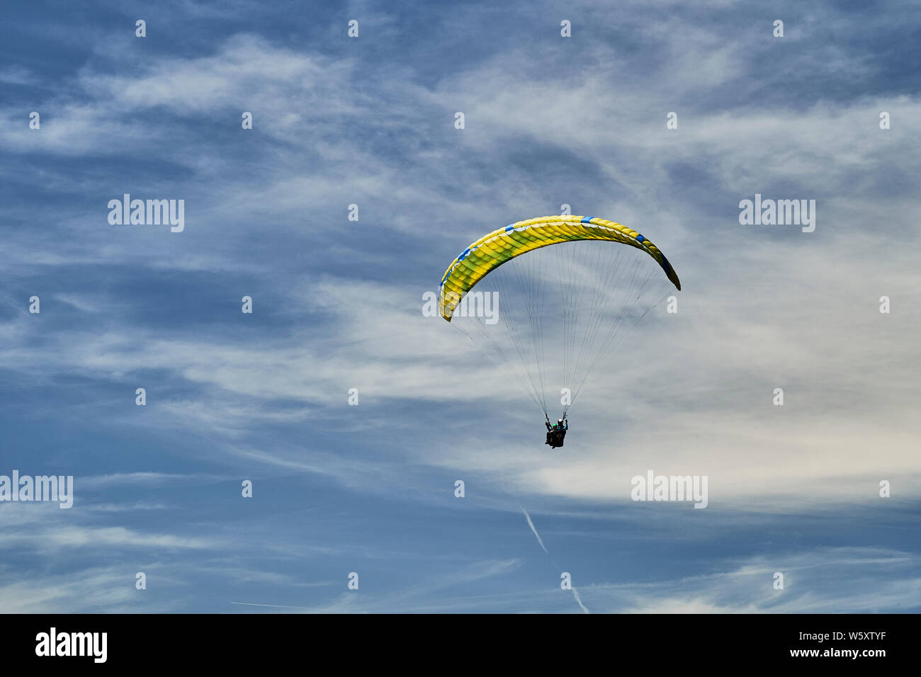 Un parapente en tandem et avec un parachute jaune et bleu et nuages de haute altitude. Banque D'Images