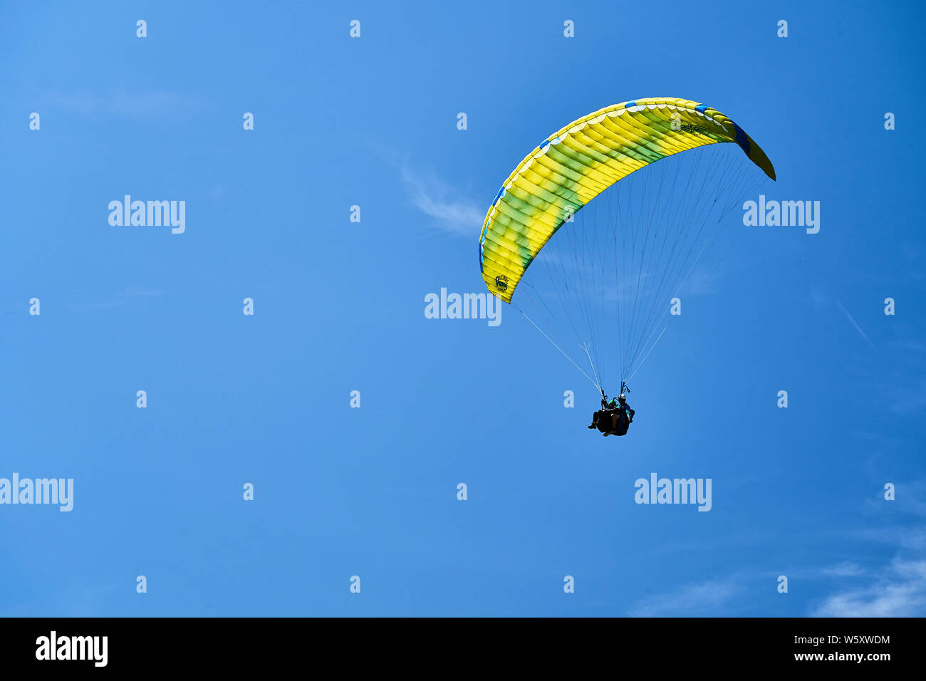 Un parapente en tandem et avec un parachute jaune et bleu et nuages de haute altitude. Banque D'Images