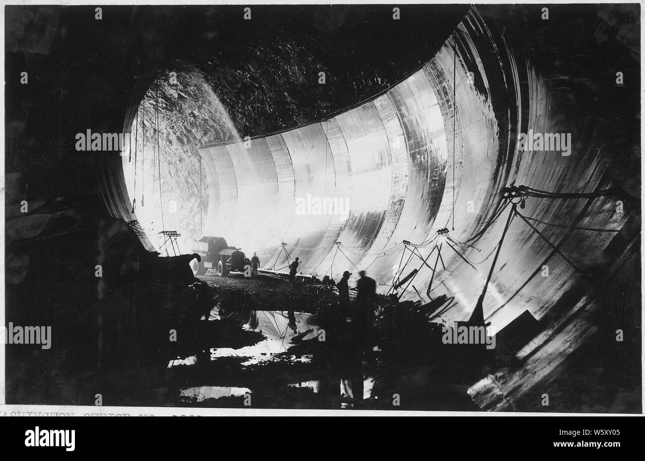 Face latérale du béton en place dans galerie de dérivation n° 3. Deux méthodes d'humidification sont affichées. Droit à l'arrosage automatique avec tuyau en plomb vu en haut du béton est en cours d'utilisation ; béton à gauche s'être mouillée par le flexible de la renverser. Note méthode de lumière et d'ancrage des câbles d'alimentation. ; Portée et contenu : la photographie de deux volumes d'une série d'albums de photos documentant la construction de barrage Hoover. Boulder City, Nevada. Banque D'Images