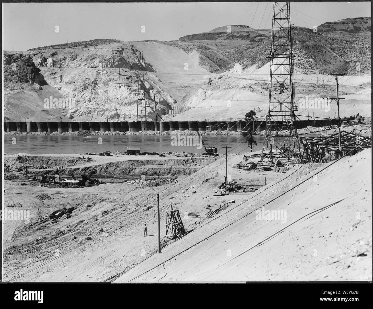 Vue depuis l'est la pente du canal de fuite est et centre - les tours du pont de suspension du convoyeur - cofferdam, et au centre de la photo est railroad trestle à l'ouest de l'usine de mélange. ; Portée et contenu : la photographie de deux volumes d'une série d'albums de photos documentant la construction du barrage de Grand Coulee et travaux connexes sur le bassin du Columbia Projet. Banque D'Images