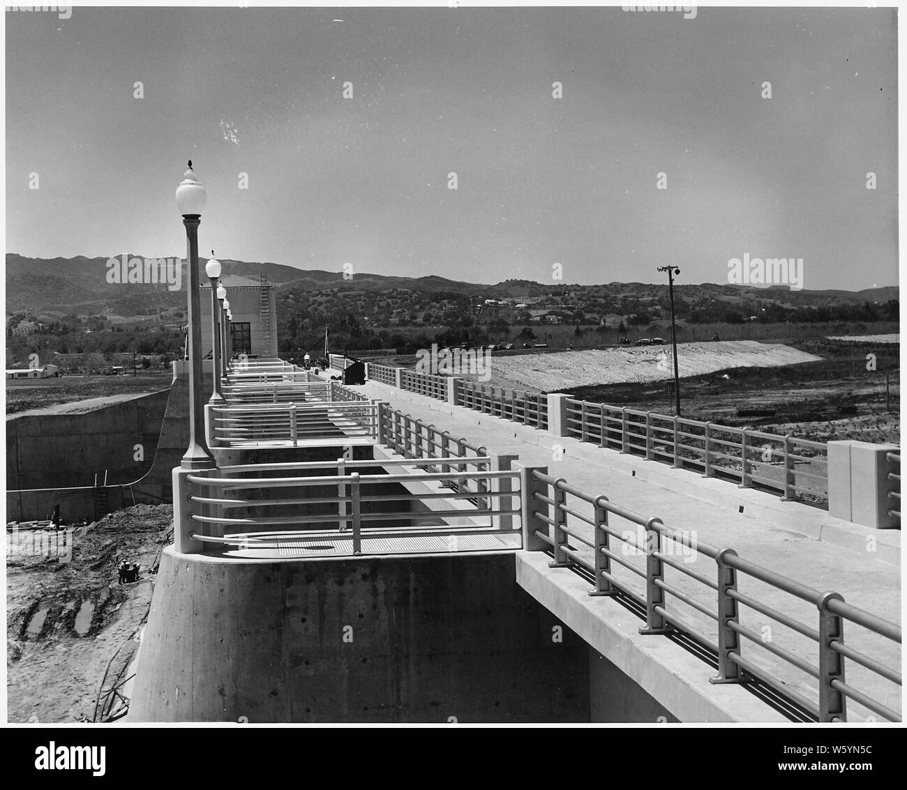 Vue de l'ouest le long du haut de l'évacuateur montrant le service pont et mains courantes. La tour de contrôle de sortie est proche de la gauche, et des travaux en cours sur une partie de l'option Inverser le remblai peut être vu dans la bonne distance. Projet : Los Angeles River Amélioration. Emplacement : Sepulveda Barrage sur Los Angeles River près de Van Nuys, nord-ouest de ville de Los Angeles, Californie. Fonds : fonds réguliers. Travaux poursuivis en vertu du contrat n° W-509-Eng.-966. ; notes générales : - Sepulveda Dam, sur la Los Angeles River dans la vallée de San Fernando. Banque D'Images