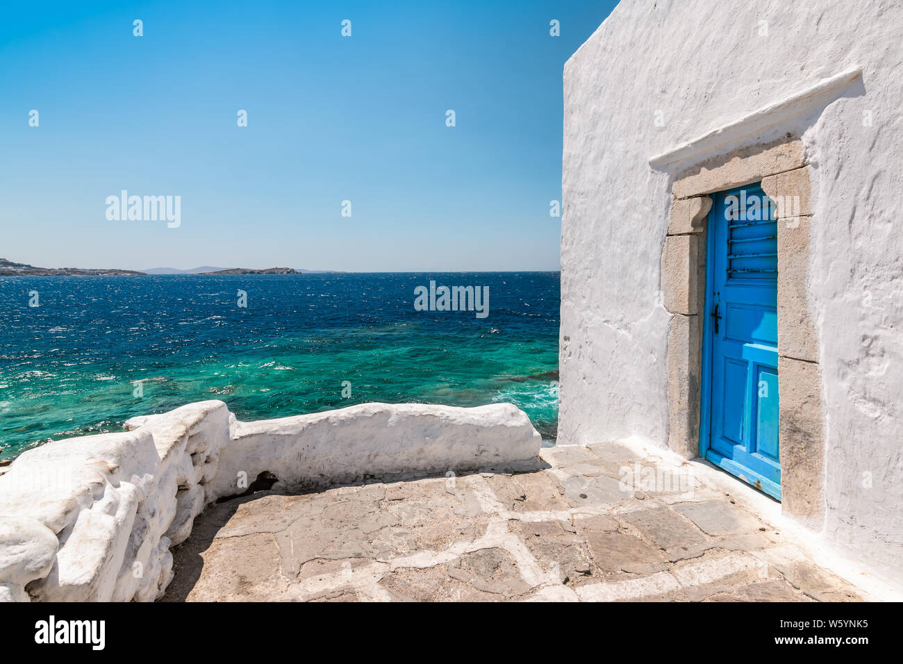 Mykonos, Grèce. Bâtiment blanc traditionnel avec porte bleue au bord de mer.. Banque D'Images