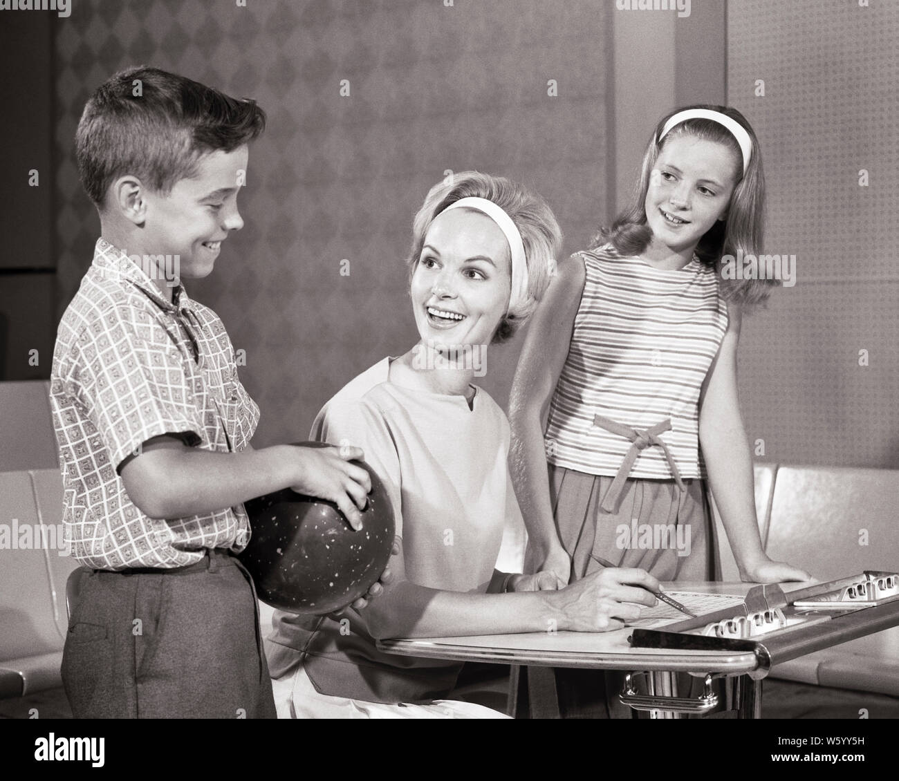 1960 Smiling maman keeping score au bowling avec la fille et le fils qui  tient une boule de bowling - s12820 HAR001 STYLE COMPÉTITION JUVÉNILE HARS  COMMUNICATION NOTE FILS HEUREUX JOIE RELIGION