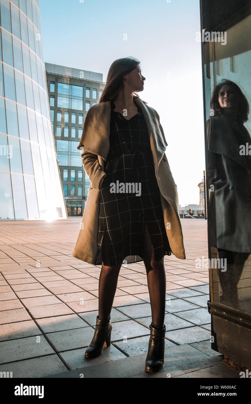 Photo d'une jeune fille dans un manteau et robe dans le contexte d'un centre d'affaires moderne, rétro-éclairage Banque D'Images