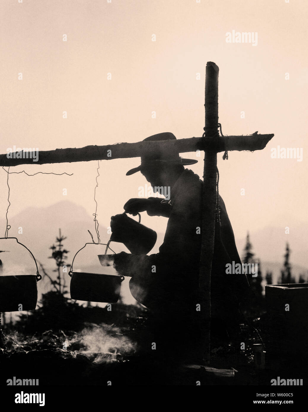 La silhouette anonyme 1930 COWBOY HOMME AGENOUILLÉ À CÔTÉ DE LA COULÉE DE FEU DE TASSE DE CAFÉ LE GLACIER NATIONAL PARK DU MONTANA USA - s5050 HAR001 HARS CONTOURS COWBOYS AVENTURE AGENOUILLÉS SILHOUETTÉ loisirs Parcs et loisirs PARC NATIONAL DES GLACIERS PAR SENTIER DE ROUGHING IT MT PARC NATIONAL ANONYME MID-ADULT MID-ADULT MAN NOIR ET BLANC HAR001 old fashioned Banque D'Images