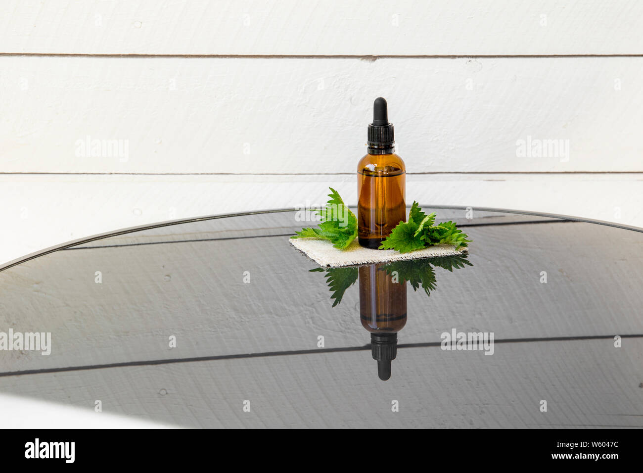 Huile essentielle d'ortie ou l'infusion en bouteille pipette médicale brun avec des branches d'orties conseil en arrière-plan. Banque D'Images