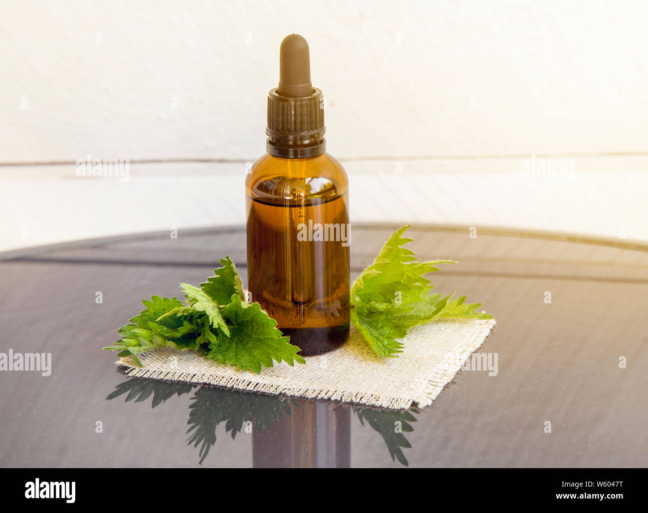 Huile essentielle d'ortie ou l'infusion en bouteille pipette médicale brun avec des branches d'orties conseil en arrière-plan. Banque D'Images