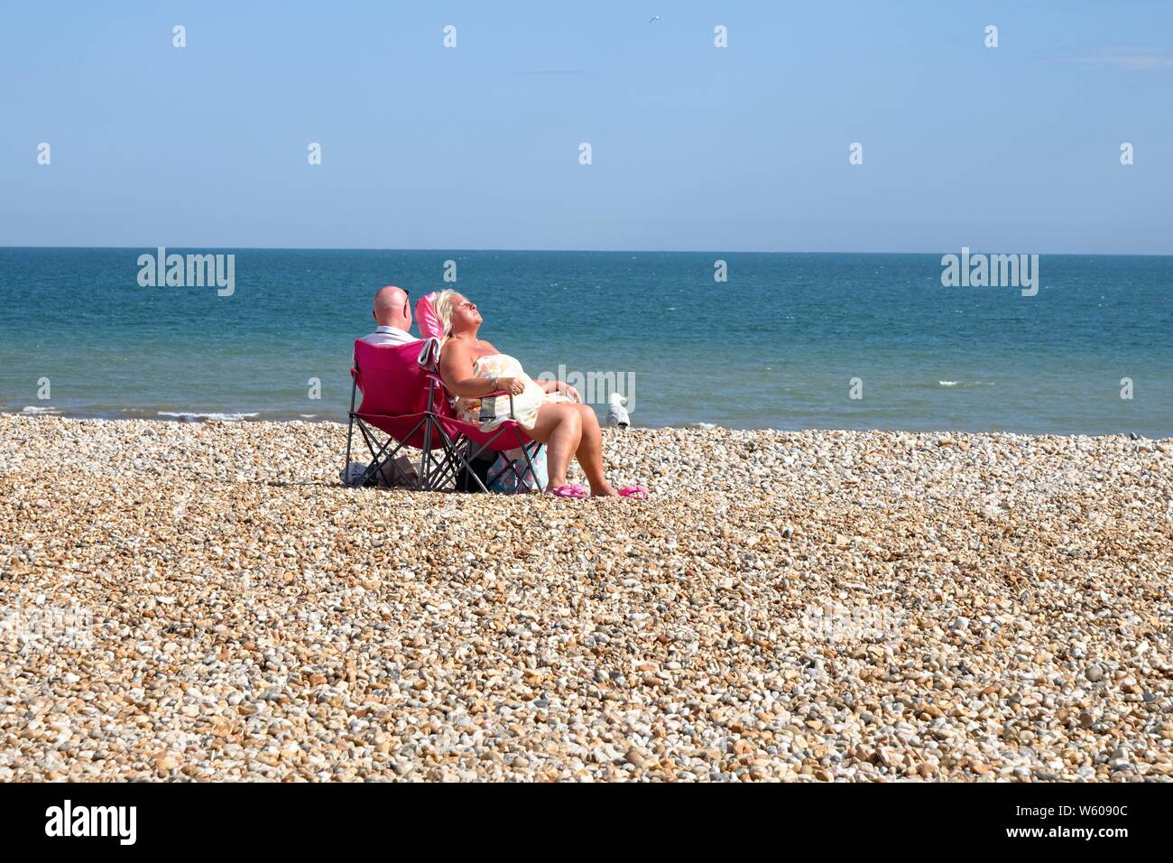 Couple de personnes âgées assis sur des chaises tout en bronzant sur une plage de Bognor Regis vide avec la mer en arrière-plan, West Sussex England UK Banque D'Images