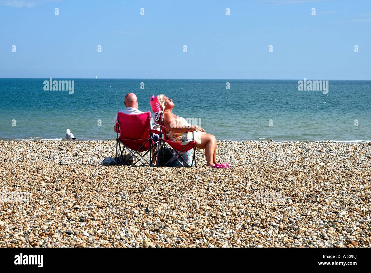 Couple de personnes âgées assis sur des chaises tout en bronzant sur une plage de Bognor Regis vide avec la mer en arrière-plan, West Sussex England UK Banque D'Images