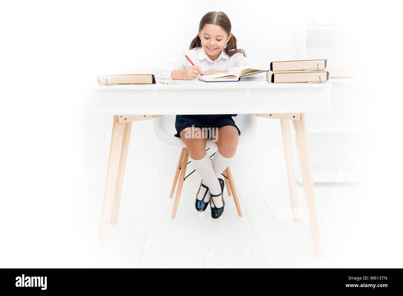 Quelle devrait être la hauteur de table d'étude. Faire ses devoirs d'écolière à table. Adorable petite fille élève étudiant au tableau arrière-plan blanc. L'étude sur 24 avec hauteur incorrecte peut entraîner des douleurs au dos. Banque D'Images