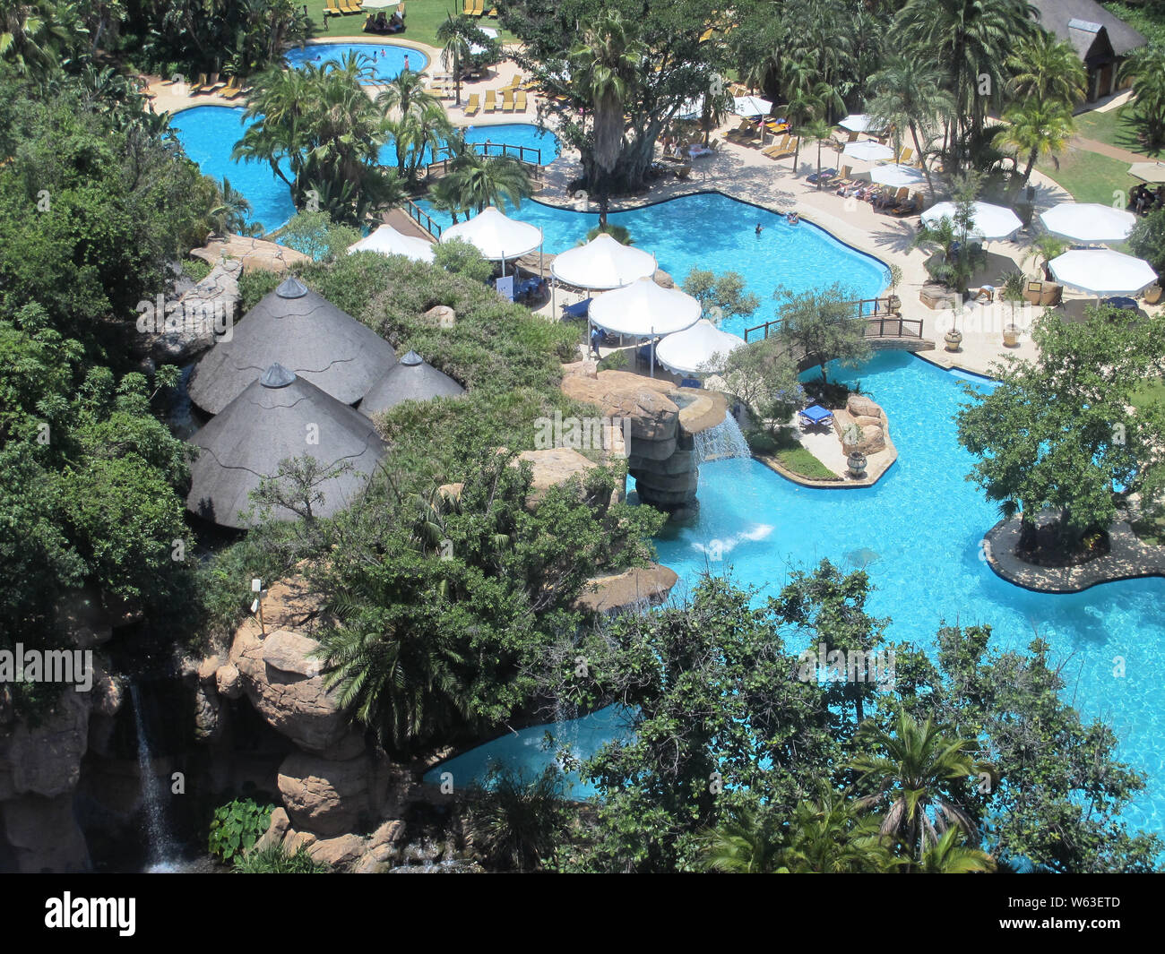 Vue aérienne ou regarder sur un hôtel resort piscine entourée par des arbres et des parasols avec de l'eau bleu turquoise à Sun City, Afrique du Sud Banque D'Images