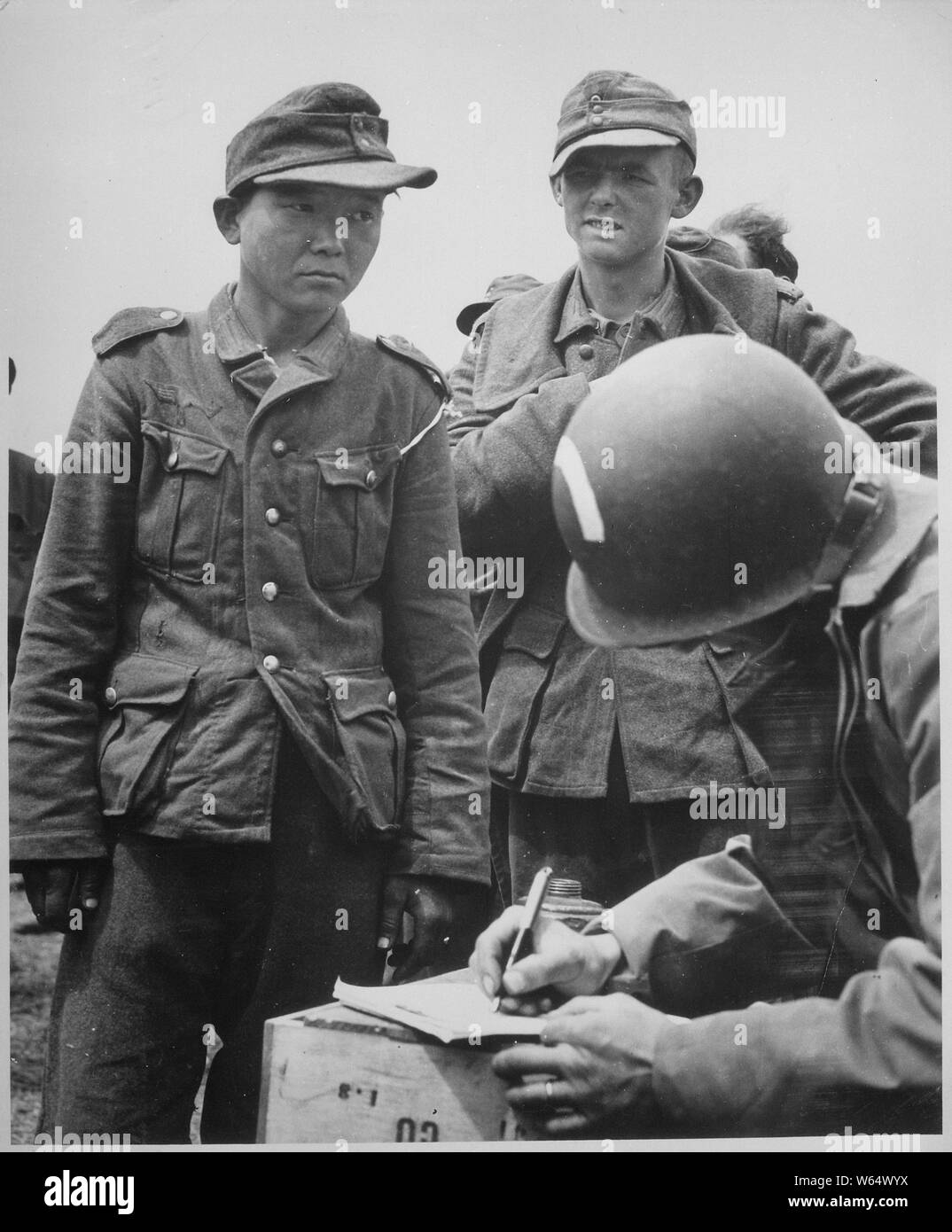La consternation et la solitude est écrit sur la face de ce jeune homme japonais, vêtu d'un uniforme nazi, dans un horizon des prisonniers allemands sur les plages de France. L'homme japonais donne son nom et son numéro à un capitaine de l'armée américaine. ; notes générales : utilisation de la guerre et des conflits Nombre 1286 lors de la commande d'une reproduction ou demande d'informations sur cette image. Banque D'Images