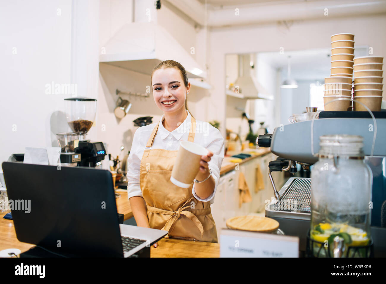 Young attractive woman smiling barista au comptoir bar, suggérant une tasse à café dans un café ou un restaurant moderne. Banque D'Images
