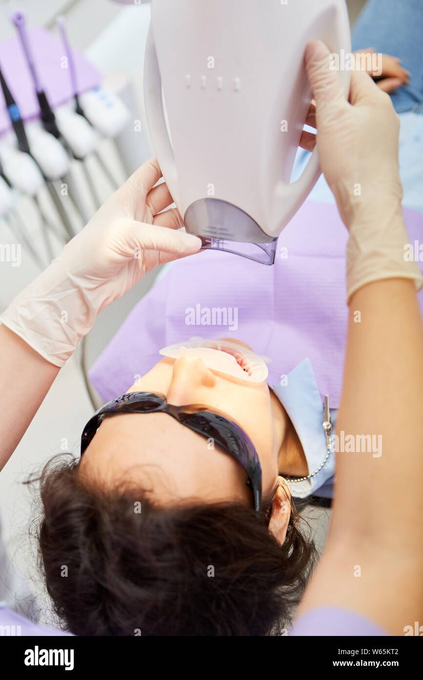 L'assistant médical ajuste la lumière lampe pour blanchiment dentaire à un patient dans le cabinet dentaire Banque D'Images