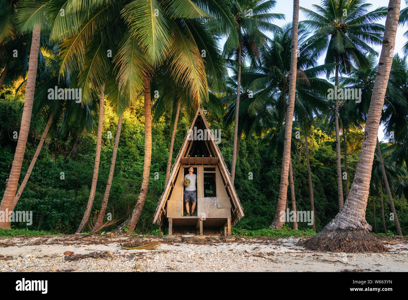 L'homme se tient à la porte de cabane et détient la noix de coco dans ses mains. La faune de la jungle à Port Barton, Philippines Banque D'Images