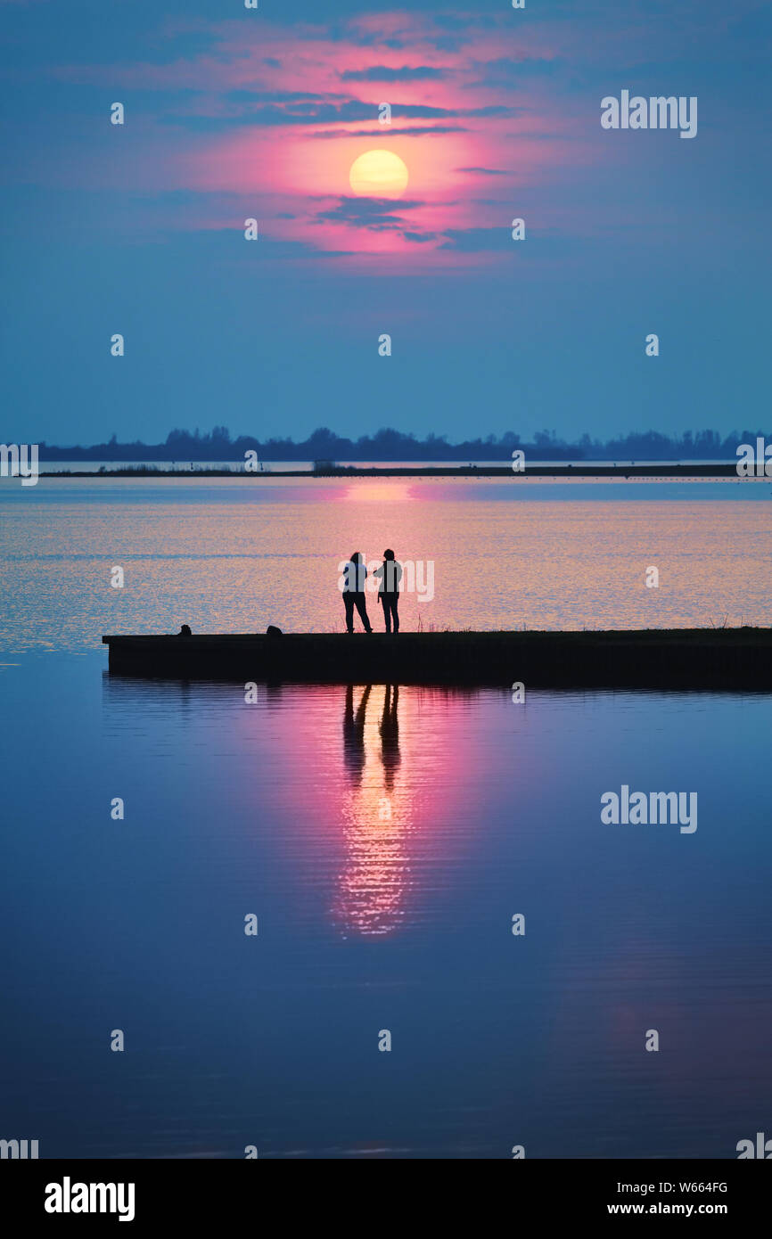 Un romantique coucher de soleil avec des gens sur une jetée au bord du lac, regardant le soleil se coucher sur un des étés chauds et colorés de droit - soir Banque D'Images