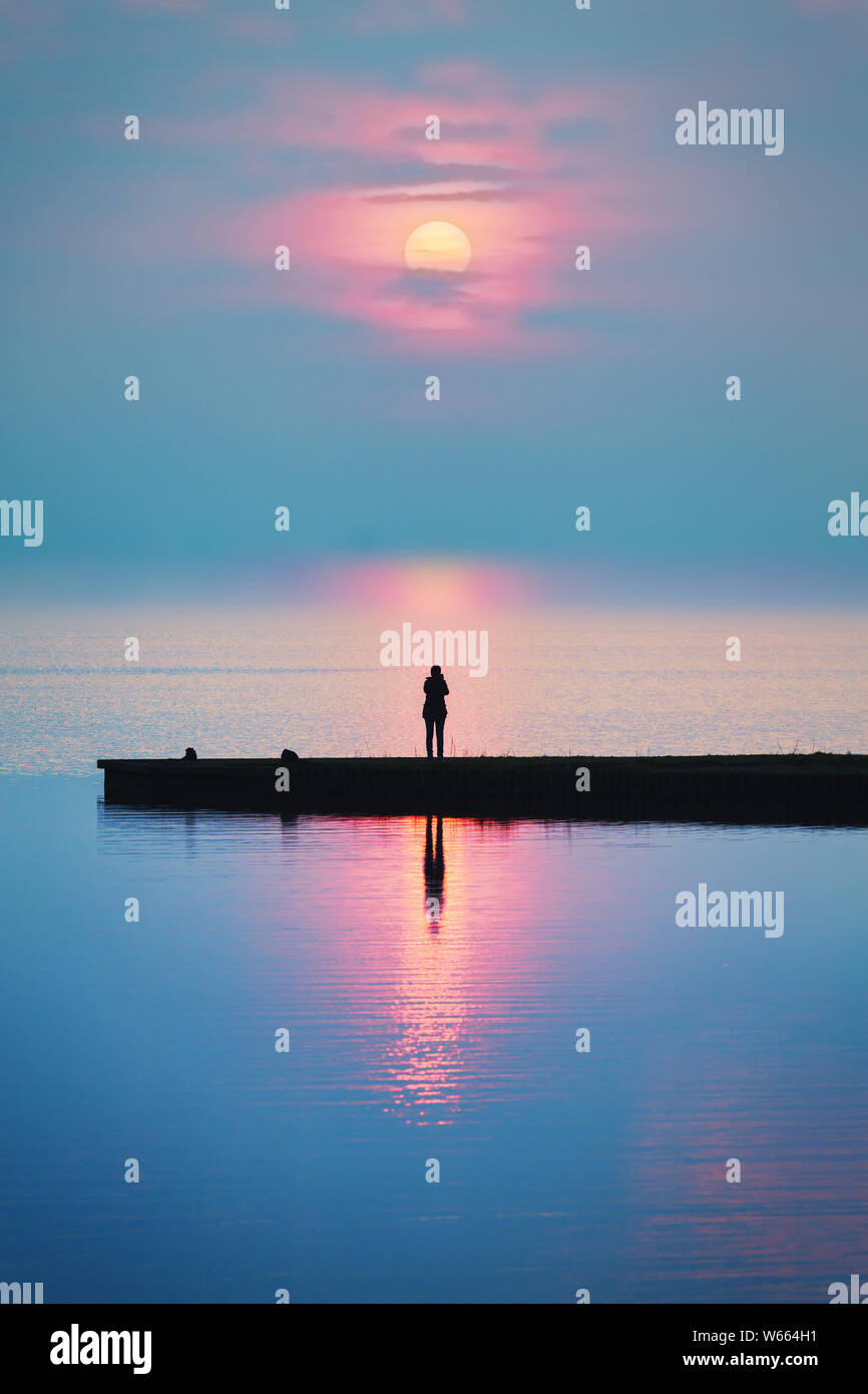 Un romantique coucher une personne sur une jetée au bord du lac en regardant le soleil se coucher sur un des étés chauds et colorés de droit - soir Banque D'Images