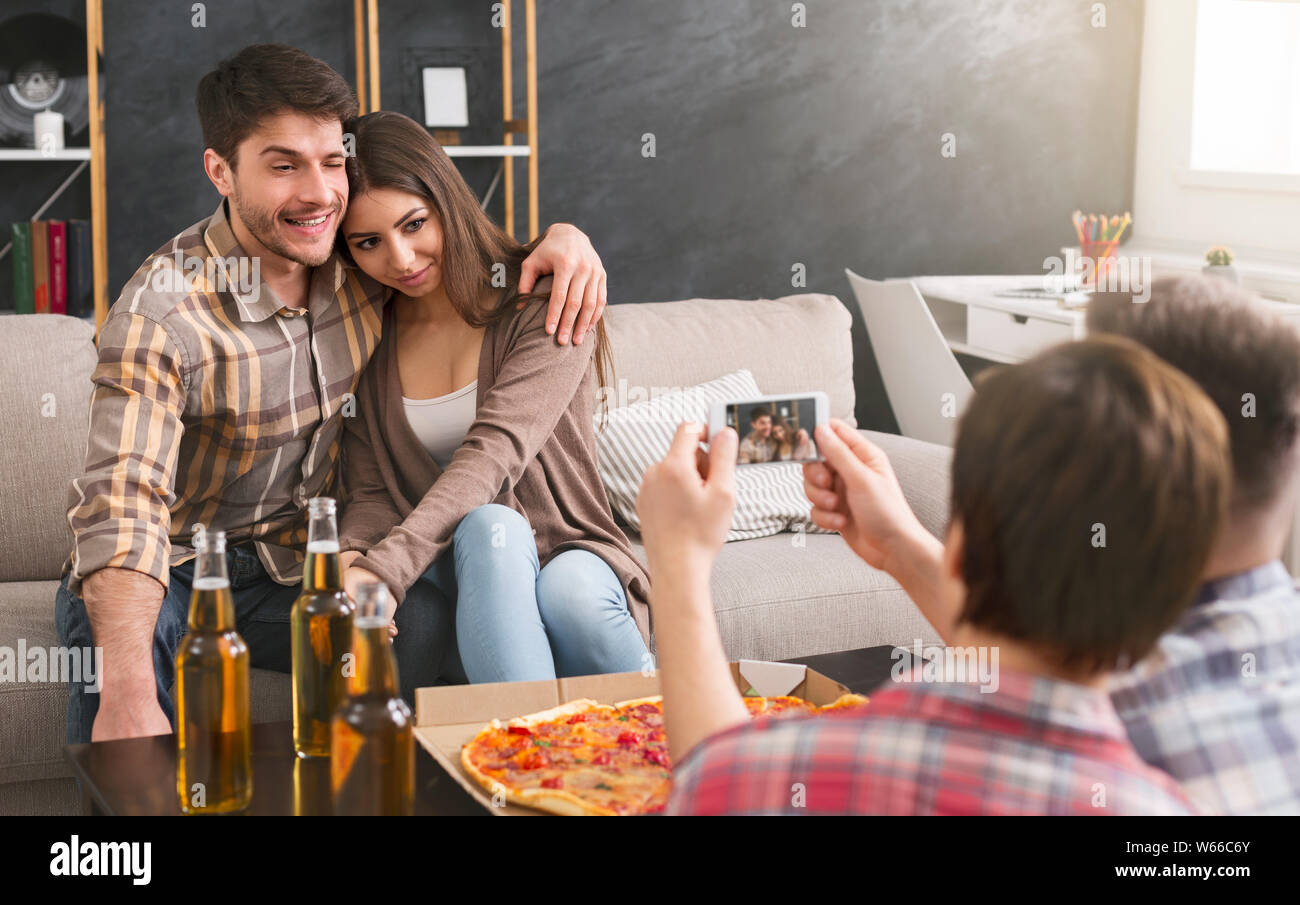 Jeune couple photographié par des amis à la maison partie Banque D'Images