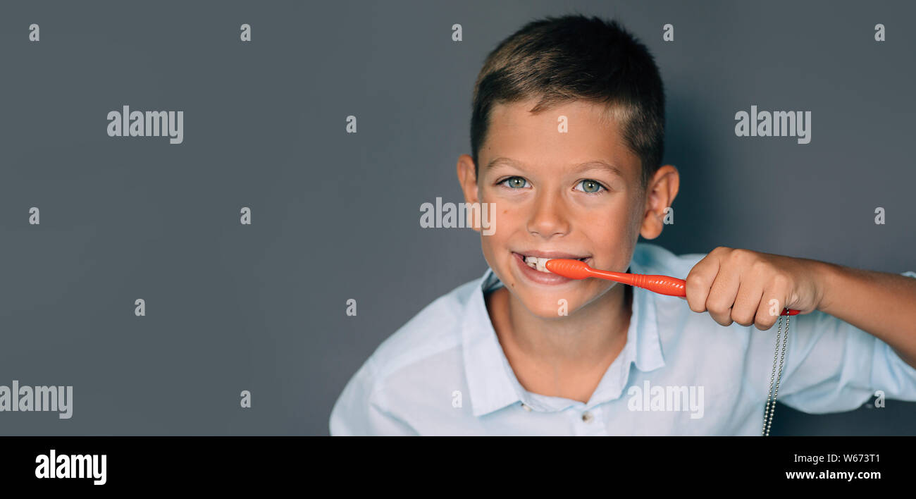 Cute boy se brosser les dents sur fond gris. Maintien de la santé et de l'hygiène des dents Banque D'Images