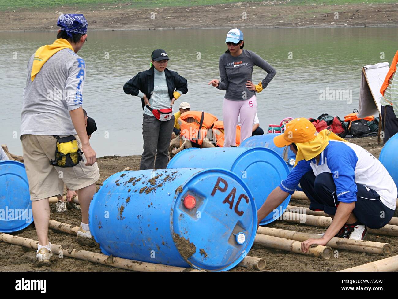 Deux jeunes femmes supervisent la fabrication d'un bateau à l'aide de tonneaux en plastique, de bâtonnets de bambou et de cordes à côté d'un barrage d'eau. Banque D'Images