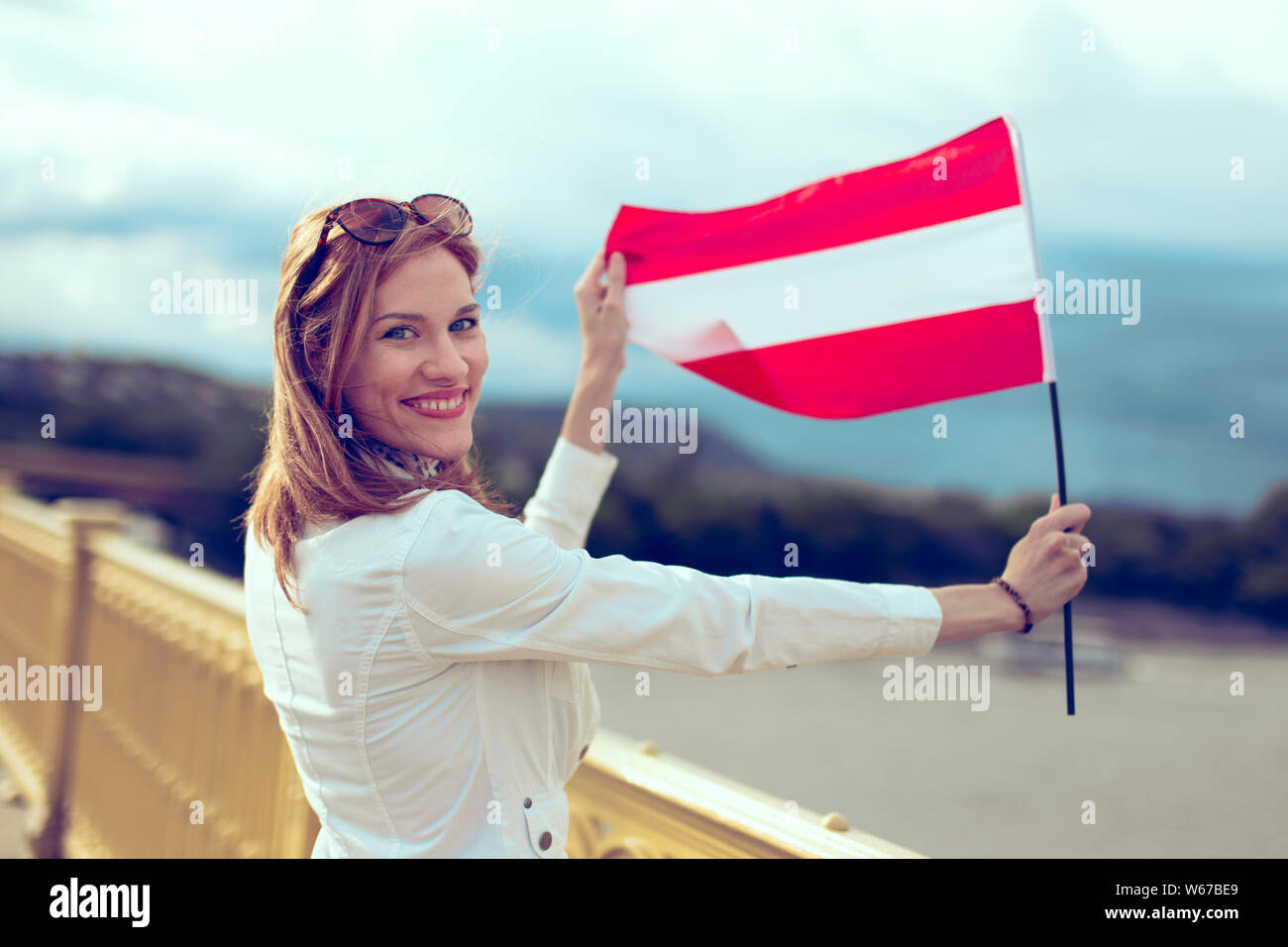 Heureux jeune rousse femme tenant un drapeau autrichien sur sourire pont Banque D'Images